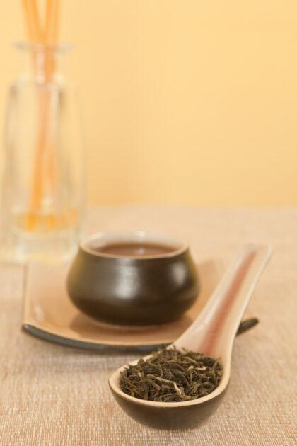 Black tea leaves on spoon, tea in tea bowl in background