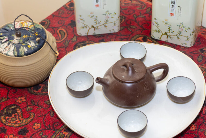 Brown clay Japanese tea set spread out on a white plate. next to traditional herbal tea in clay pots and tin cans.