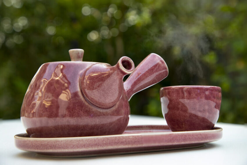 A beautiful, set of Japanese style, purple ceramic tea pot and tea cup. Blurry garden background.