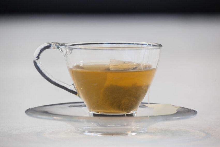 Green tea with tea bag in cup against white background