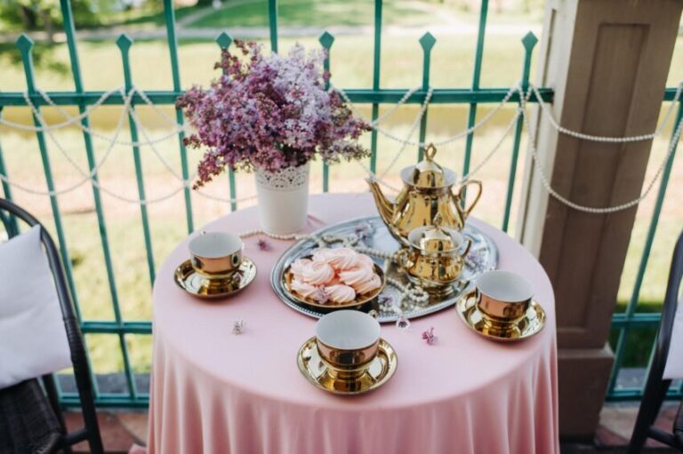 Delicate morning tea table setting with lilac flowers, antique spoons and dishes on a table with a pink tablecloth