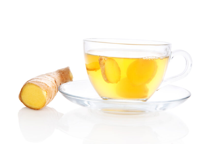 Delicious ginger tea in transparent tea cup with saucer and ginger root and ginger slices isolated on white background. 