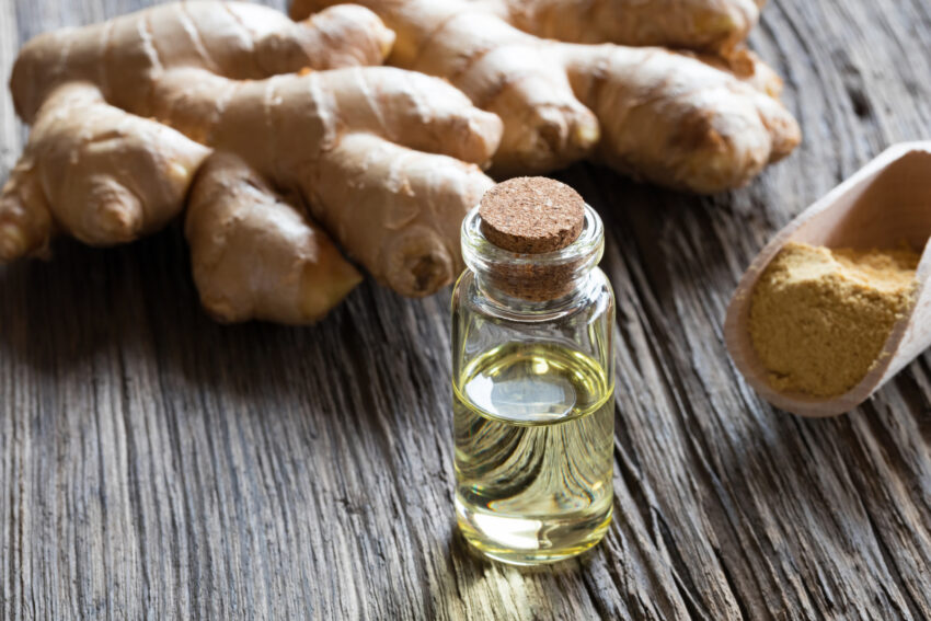 A bottle of ginger essential oil with ginger root and ground ginger