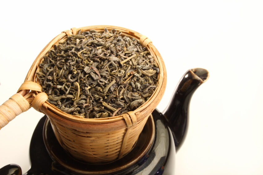 Green tea leaves in bamboo tea strainer on a tea pot.