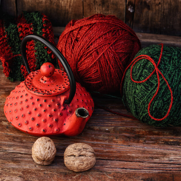 Stylish teapot with warm tea and balls of wool to knit