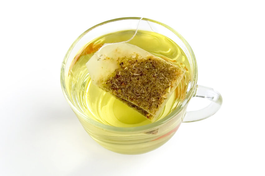The bag of green herbal tea in a glass bowl with water, isolated on a white background